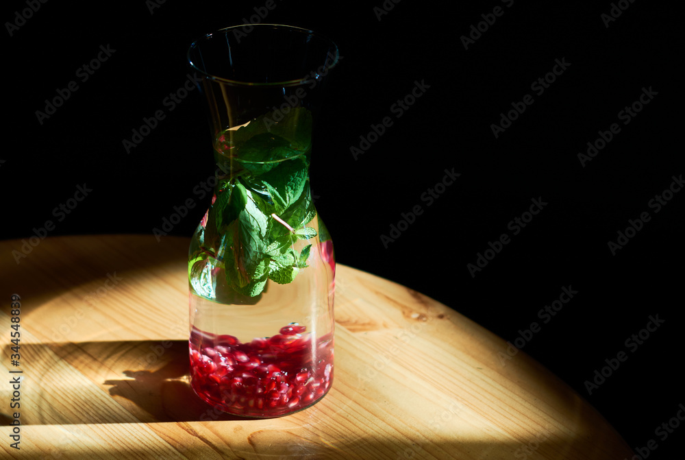 Black background and glass, drink with mint and pomegranate beans, stands opposite suns rays. Useful water. Black background and glass, drink with mint and pomegranate beans, stands opposite suns rays. Useful water.