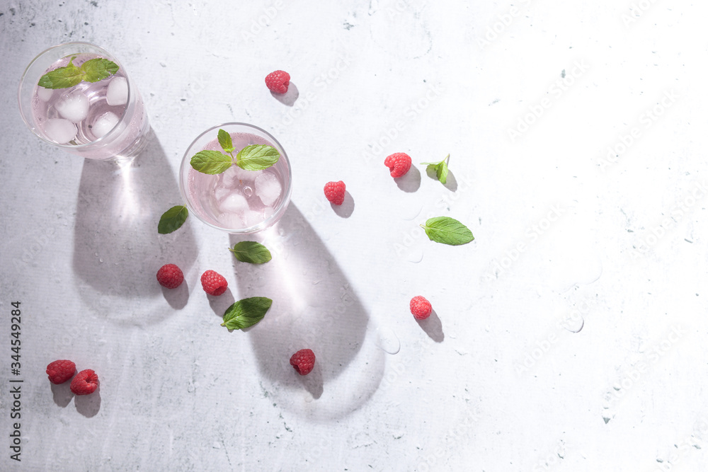 Glasses of raspberry infused water with raspberries, ice and fresh mint leaves on concrete background stone strong light with glass shadows. Copy space. Glasses of raspberry infused water with raspberries, ice and fresh mint leaves on concrete background stone strong light with glass shadows. Copy space.