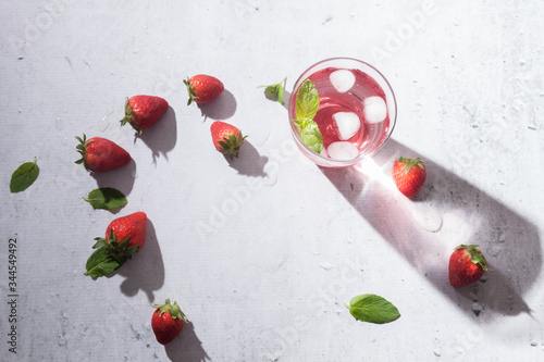 Glasses of strawberry infused water with strawberries, ice and fresh mint leaves on concrete background stone strong light with glass shadows. Copy space. Flatlay, top view.