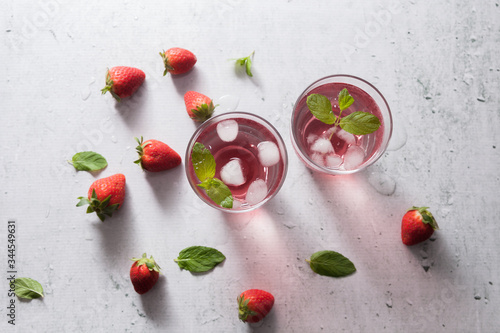 Glasses of strawberry infused water with strawberries, ice and fresh mint leaves on concrete background stone strong light with glass shadows. Copy space. Flatlay, top view.