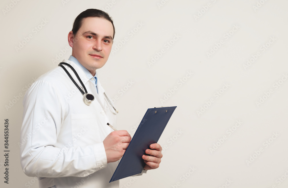 portrait of a young smiled doctor in a dressing gown, with a stethoscope and a clipboard. portrait of a young smiled doctor in a dressing gown, with a stethoscope and a clipboard.