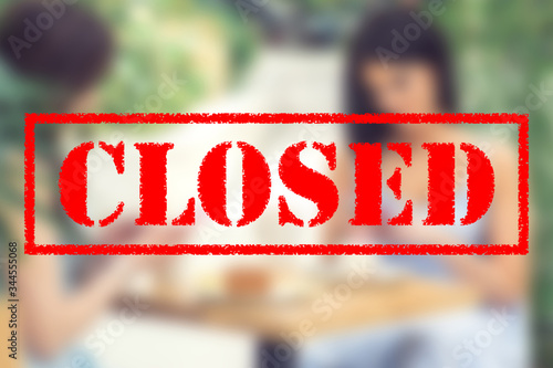 Word CLOSED on blurred background of two young women in the cafe outdoors. Coronavirus quarantine. Closed cafe outdoors.