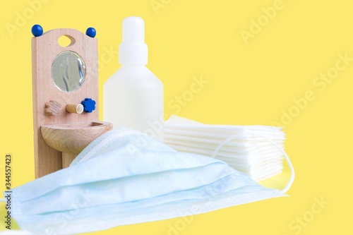 Wooden toy washbasin and anti-bacterial disinfectants in white vials on yellow. Concept personal hygiene during pandemic coronavirus. Frequent and thorough hand washing photo