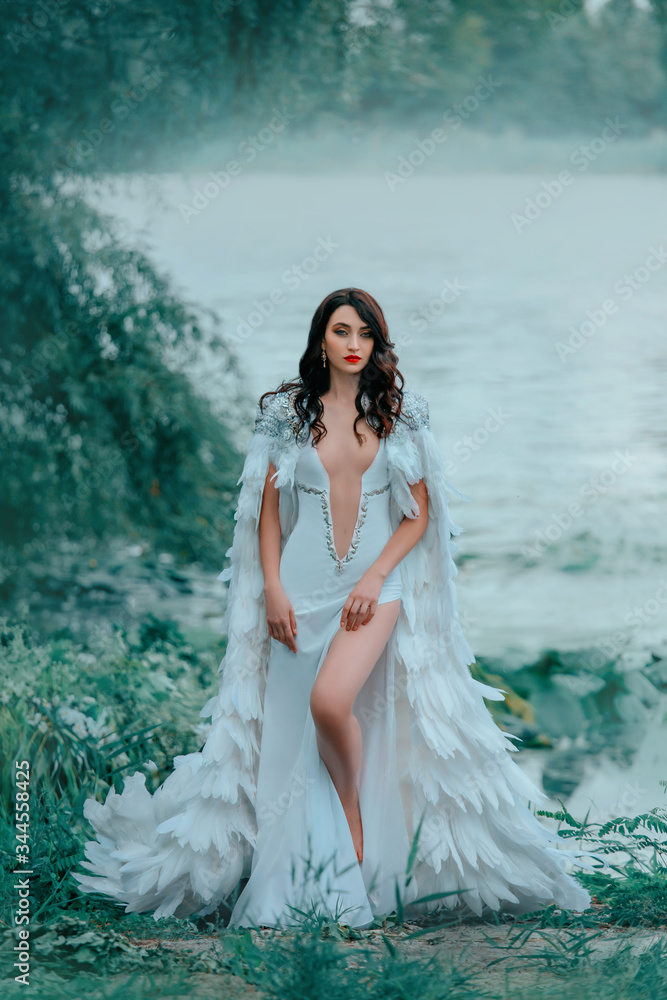 woman queen in luxury white vintage dress sexy neckline. Medieval fantasy  lady swan goddess. Image princess gothic cloak cape creative fashion  feather design. Model posing bare legs. Summer lake river Stock Photo