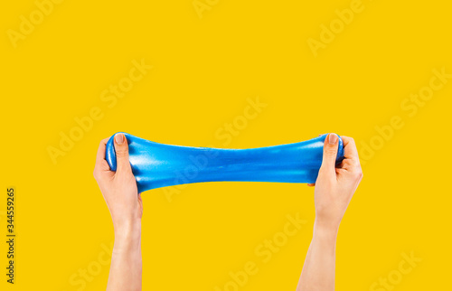 Blue slime stretchable toy for children in hands. An elastic antistress toy for relaxation. Hands gum. Funny Games. Slime on yellow background. Copy space, place for text. photo