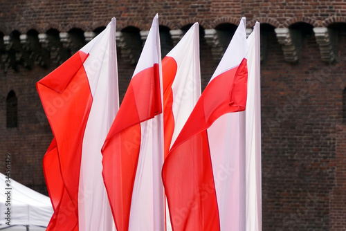 Polish red and white flags in old town in front of building on a Sunny day. red brick wall on background. 1 of May, November 11, flag or independence or labor day. Government holiday in poland.