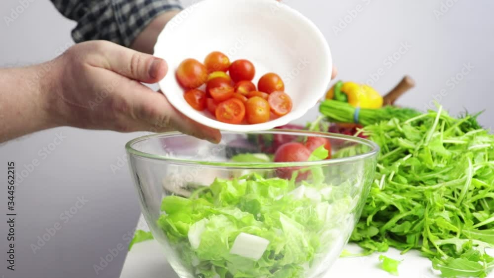 male chef hands add chili tomatoes to a bowl with lettuce leaves, salad preparation, healthy food, vegetarian. male chef hands add chili tomatoes to a bowl with lettuce leaves, salad preparation, healthy food, vegetarian.