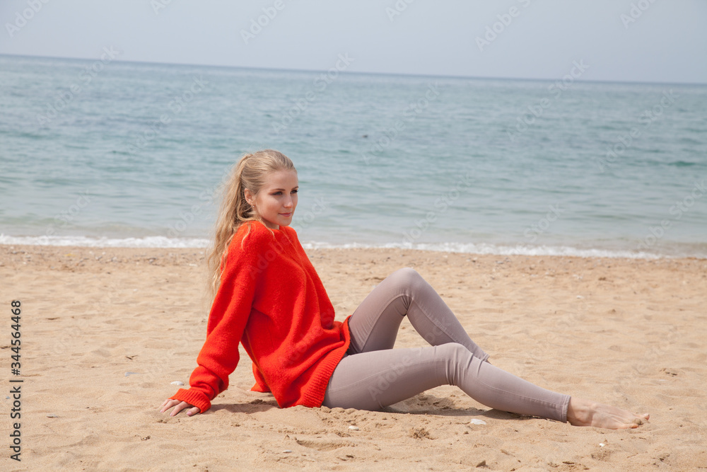 Beautiful blonde woman sits alone on a sandy beach by the sea Beautiful blonde woman sits alone on a sandy beach by the sea