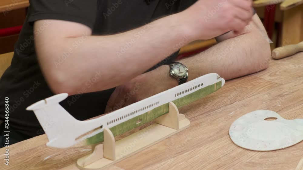 man colours wooden outdated jetliner model fuselage edge standing on support with small brush at table slow motion closeup man colours wooden outdated jetliner model fuselage edge standing on support with small brush at table slow motion closeup