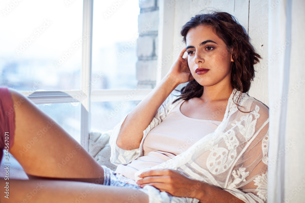 young pretty brunette woman sitting at window at home at morning relaxing, lifestyle people concept young pretty brunette woman sitting at window at home at morning relaxing, lifestyle people concept