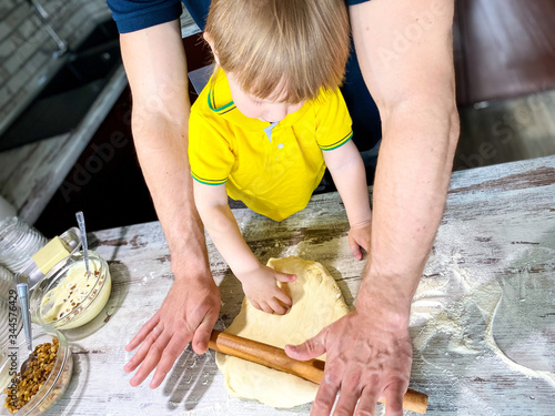 A fair-skinned little child with his father / grandfather prepares sweet rolls filled with cottage cheese and raisins in the kitchen at home. A step-by-step cooking process.Defocus light background.