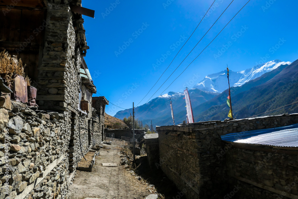 A row of stony buildings in Manang, Annapurna Circus Trek, Himalayas, Nepal, with the view on Annapurna Chain and Gangapurna. Dry and desolated landscape.  High mountain peaks, covered with snow.