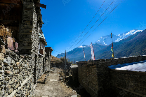 A row of stony buildings in Manang, Annapurna Circus Trek, Himalayas, Nepal, with the view on Annapurna Chain and Gangapurna. Dry and desolated landscape. High mountain peaks, covered with snow.