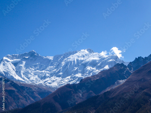 A close up view on snow caped Himalayan peak seen from Annapurna Circuit Trek, Nepal. Sharp and steep slopes of the mountain. Powder snow being blown by strong wind. First sunbeams reaching the peak