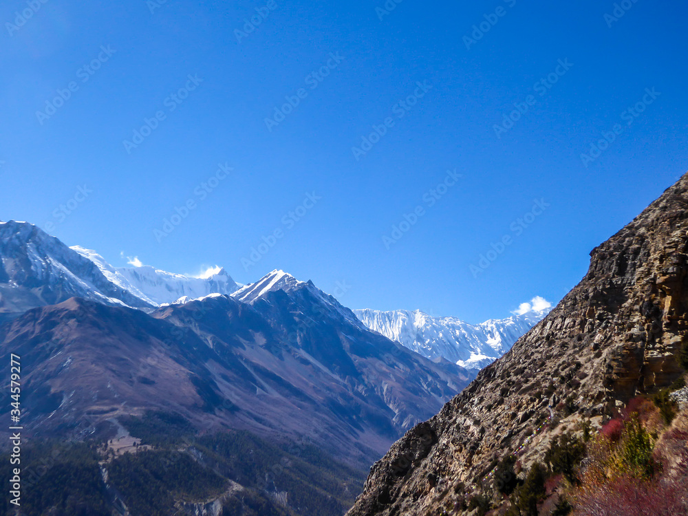 A panoramic view on Manang valley from Praken Gompa, Nepal. High Himalayan ranges around. Some dried bushes on the sides. Snow capped peaks of Annapurna Chain. Harsh landscape.