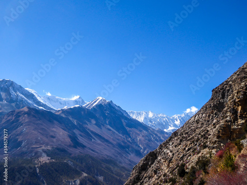 A panoramic view on Manang valley from Praken Gompa, Nepal. High Himalayan ranges around. Some dried bushes on the sides. Snow capped peaks of Annapurna Chain. Harsh landscape.