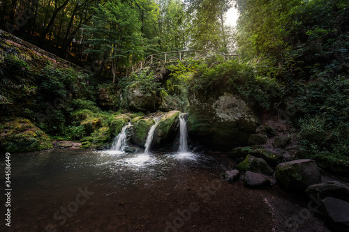 Mystical forest shot with bridge over cascade waterfalls in Luxembourg - the three small waterfalls known as Schiessentuempel in Mullerthal  Luxembourg  also known as Little Switzerland 