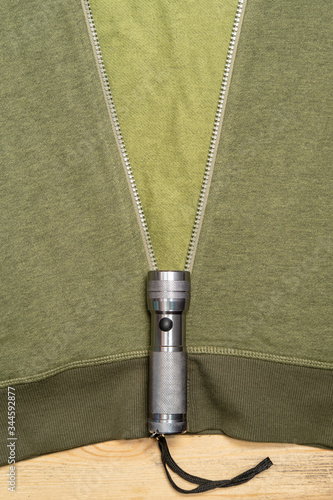 Fototapeta Naklejka Na Ścianę i Meble -  Sweatshirt on which lies a flashlight from which there is an unfastened zipper, as if rays of light. Creative idea. Vertical photo.