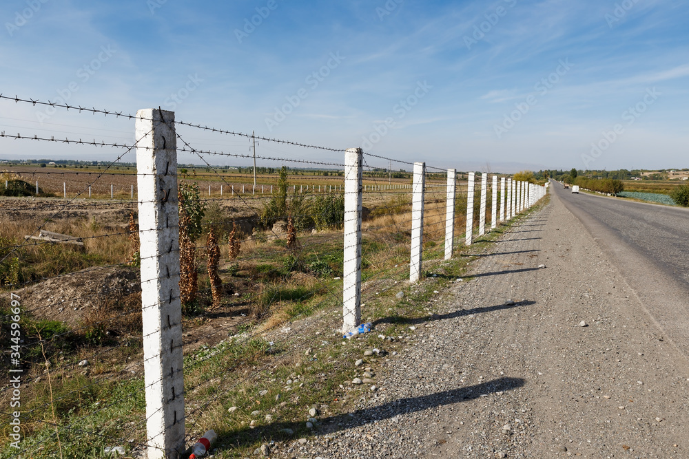 state border between Kyrgyzstan and Uzbekistan, road along a barbed wire fence.