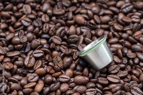 Reusable metal coffee capsule on the dark roasted coffee bean.