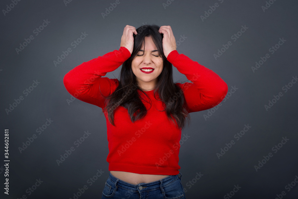 Exasperate female keeps hands on temples, feels strong headache, closes eyes with pain, need healthy sleep, being overworked, fatigue and tired. Europea woman being ill, isolated over gray background