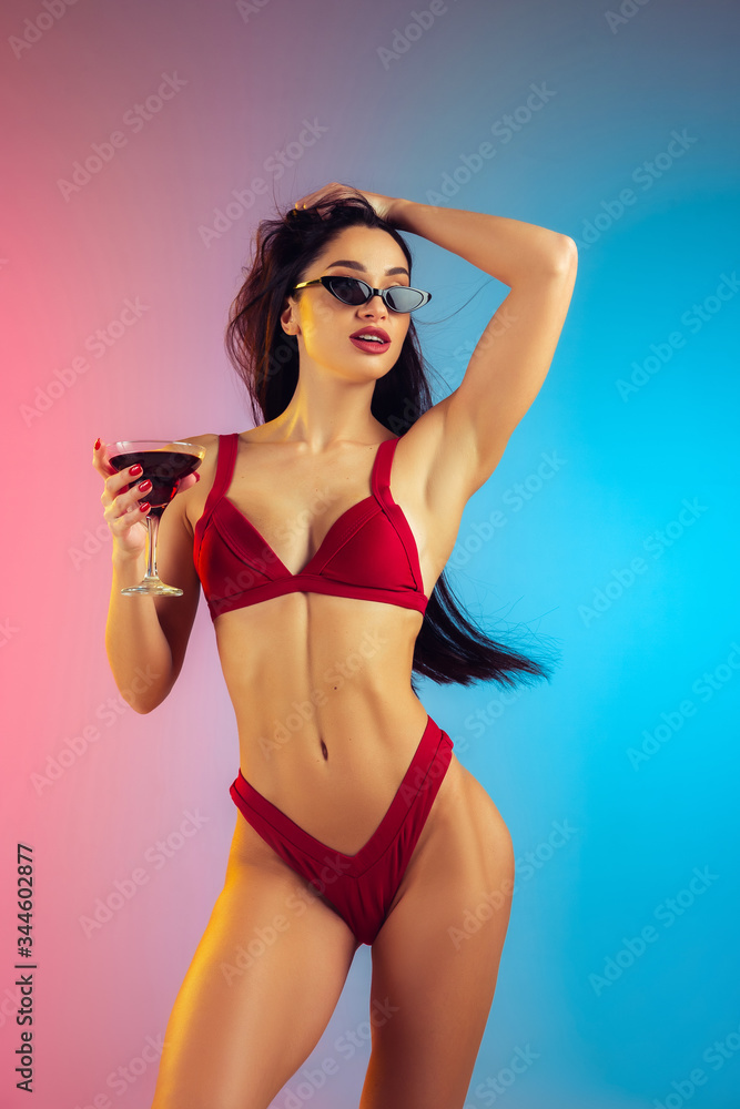 Fashion portrait of young fit and sportive caucasian woman in stylish red swimwear on gradient background. Brunette longhair model. Perfect body ready for summertime. Beauty, resort, sport concept.