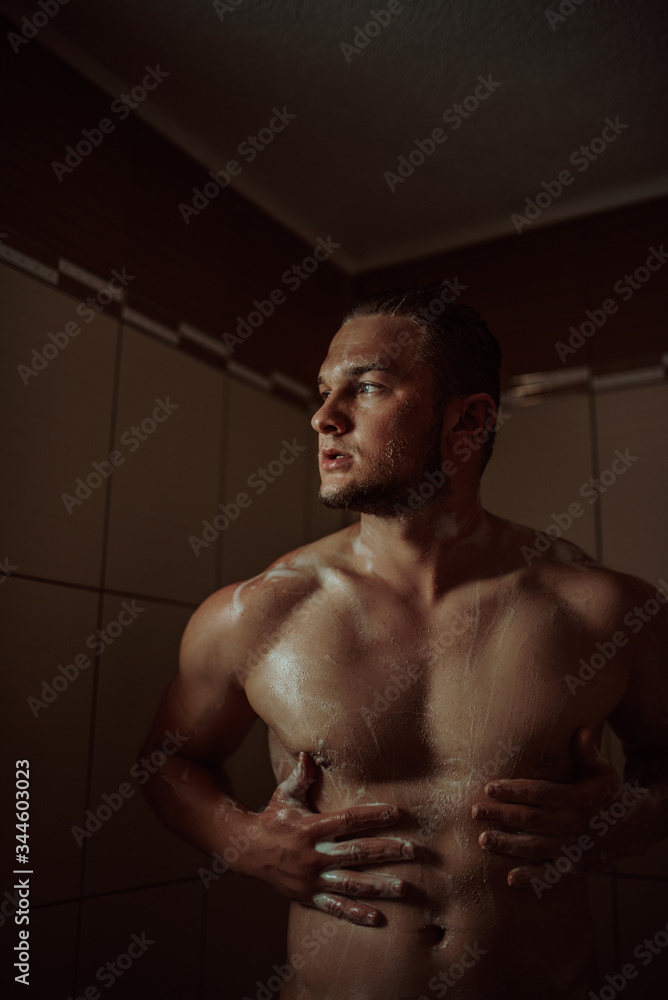 Athletic good looking and attractive man with muscular body standing under running water in shower room Athletic good looking and attractive man with muscular body standing under running water in shower room