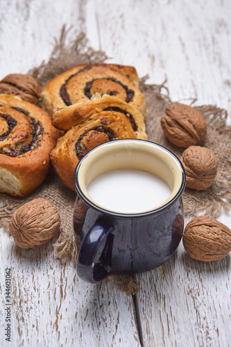 Basket of homemade buns with jam, served on old wooden table with walnuts and cup of milk