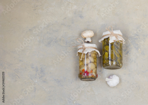 Fermented mushrooms and gherkins, cucumbers in a glass jar on a light background.