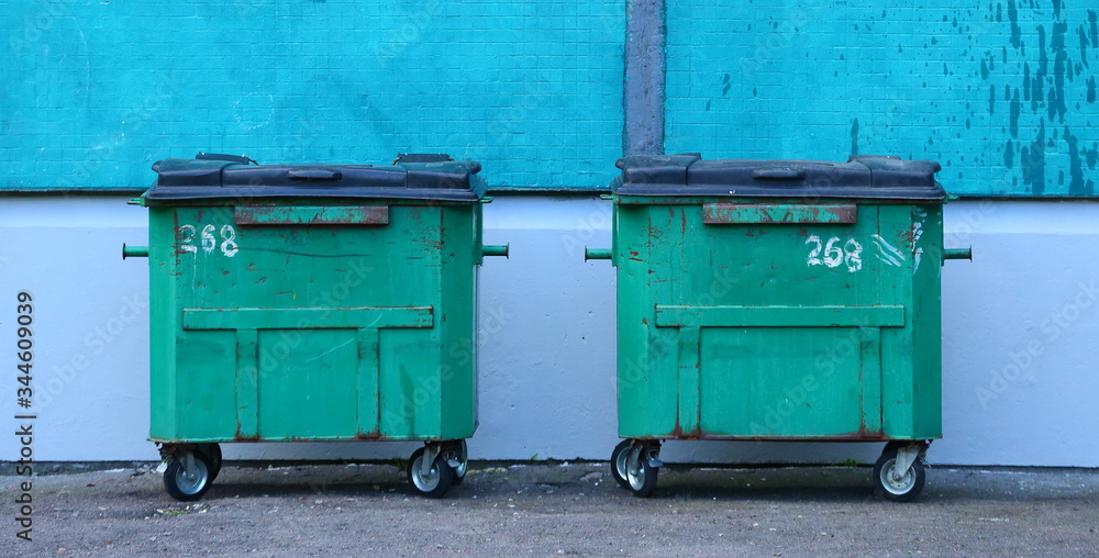 Green plastic dumpsters on wheels against the wall of the house