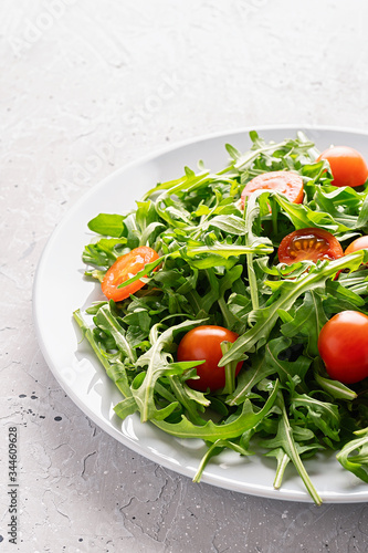 Fresh salad with arugula and cherry tomatoes on a plate on gray background. Healthy food. Copy space