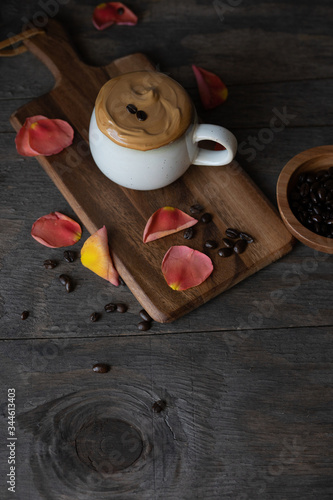 A cup of Dalgona coffee on a wooden table with coffee beans and petals. Trendy fluffy whipped coffee