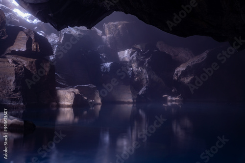 Underground lake in a hidden cave under a rocky mountain. The small rays of sunlight peaking in reflects the rock against the smoot water surface.