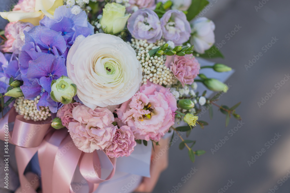 Flower arrangement in a pink hat box was created by a florist for a wedding gift. Flower bouquet of blue hydrangea, white Freesia, pink Ranunculus asiaticus, eustoma flowers, roses and eucalyptus