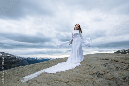 a bride in a long wedding dress on a rock fragment in the mountains