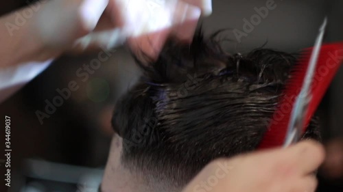 Barber makes a male haircut with a professional scissors and a comb in a barbershop on light background, close-up.