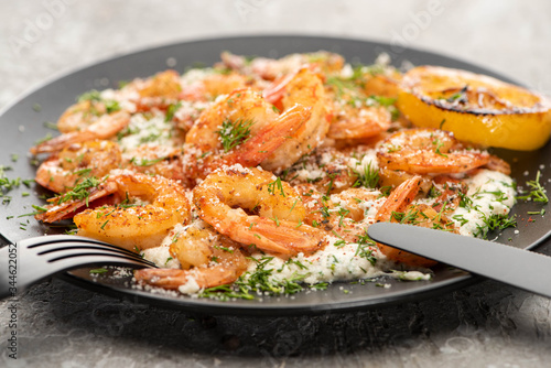 selective focus of fried shrimps in sauce with dill and lemon in black plate on grey concrete background with cutlery
