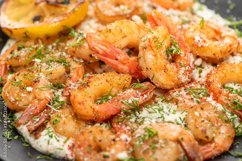 close up view of fried shrimps in sauce with dill and lemon in black plate close up view of fried shrimps in sauce with dill and lemon in black plate