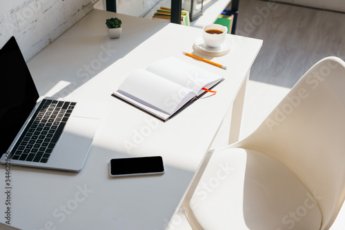 home office with smartphone, notepad, coffee cup and laptop on table in sunlight
