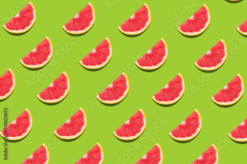 Flat lay fruit pattern of fresh grapefruit slices on green background.