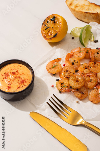 Konstfotografi fried shrimps on parchment paper with sauce and lime near golden cutlery on whit