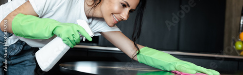 happy girl in latex gloves cleaning table with rag and spray bottle  horizontal crop