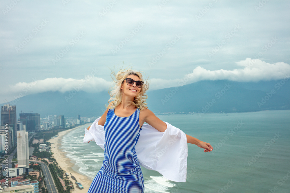Woman young adult in a dress on the roof of a building with a view of the city's seascape on a Sunny day