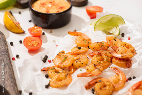 selective focus of fried shrimps with sauce, lime and pepper on white parchment paper