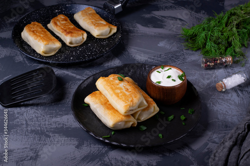 Pancakes with filling are served on the black plate with sour cream and topped with green onion