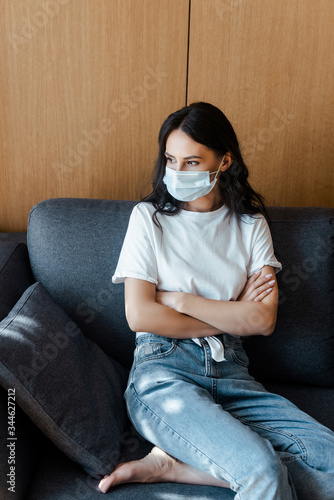 attractive woman with crossed arms in medical mask sitting at home on self isolation