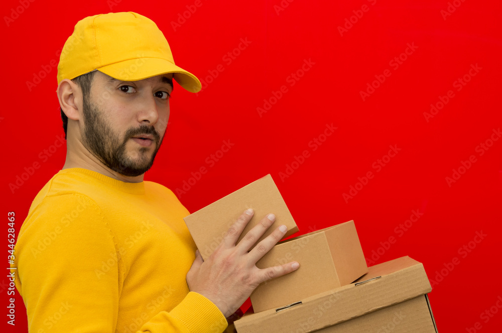 Delivery man employee in yellow cap blank t-shirt uniform face mask gloves hold empty cardboard box isolated on red background studio Service quarantine pandemic coronavirus virus 2019-ncov concept. Delivery man employee in yellow cap blank t-shirt uniform face mask gloves hold empty cardboard box isolated on red background studio Service quarantine pandemic coronavirus virus 2019-ncov concept.