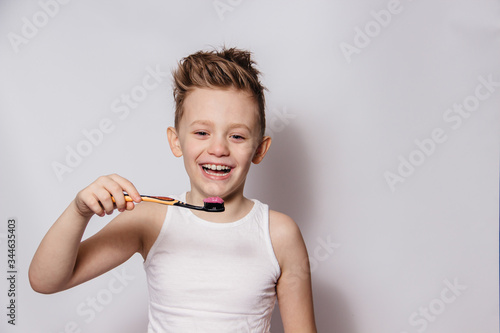 The boy brushes his teeth and laughs on a white background
