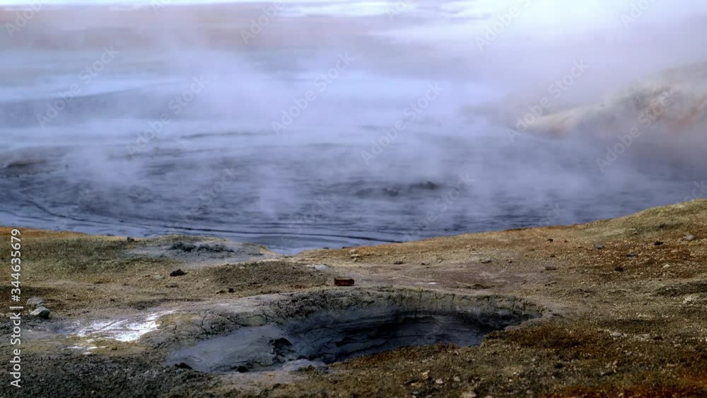 Smoke steaming from a hole in the ground near a geothermal spring in Iceland. A hot pool of natural boiling water is seen behind it. Smoke steaming from a hole in the ground near a geothermal spring in Iceland. A hot pool of natural boiling water is seen behind it.