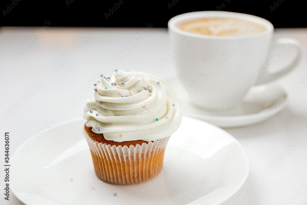 A delicious vanilla cupcake with cream and a cup of cappuccino coffee. Soft focus photo A delicious vanilla cupcake with cream and a cup of cappuccino coffee. Soft focus photo
